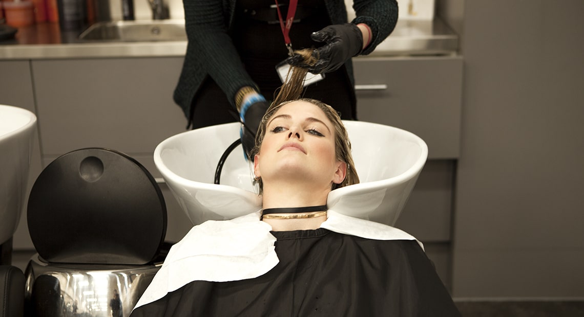 Жена с глава поставена на фризьорска мивка, чиято коса се изплаква от фризьор